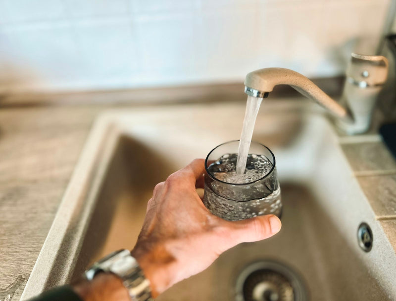 Hand filling a glass with water from a kitchen tap