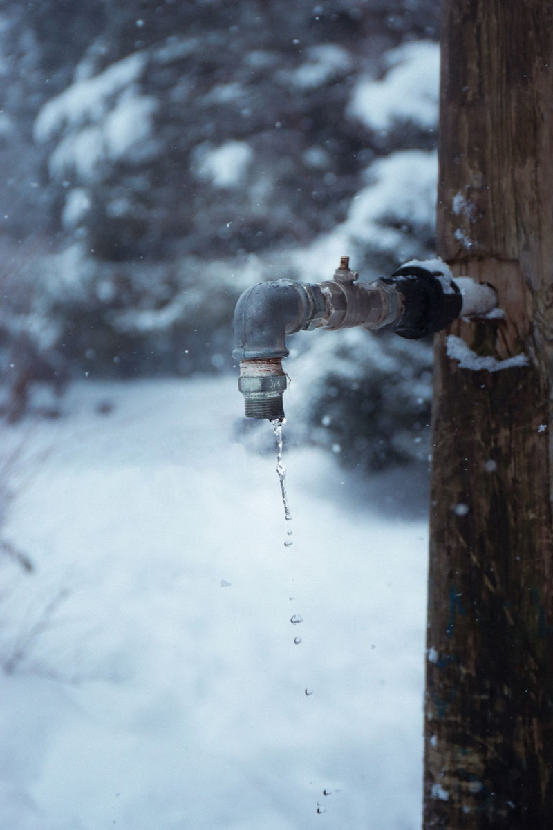 Outdoor water tap on a post dripping in falling snow