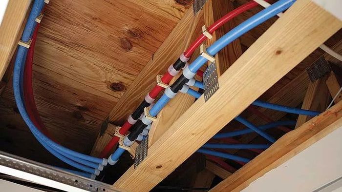 Red and blue PEX water lines run through floor joists with manifold fittings