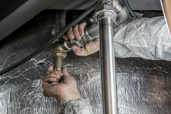 Hands tightening a brass fitting on a metal water pipe