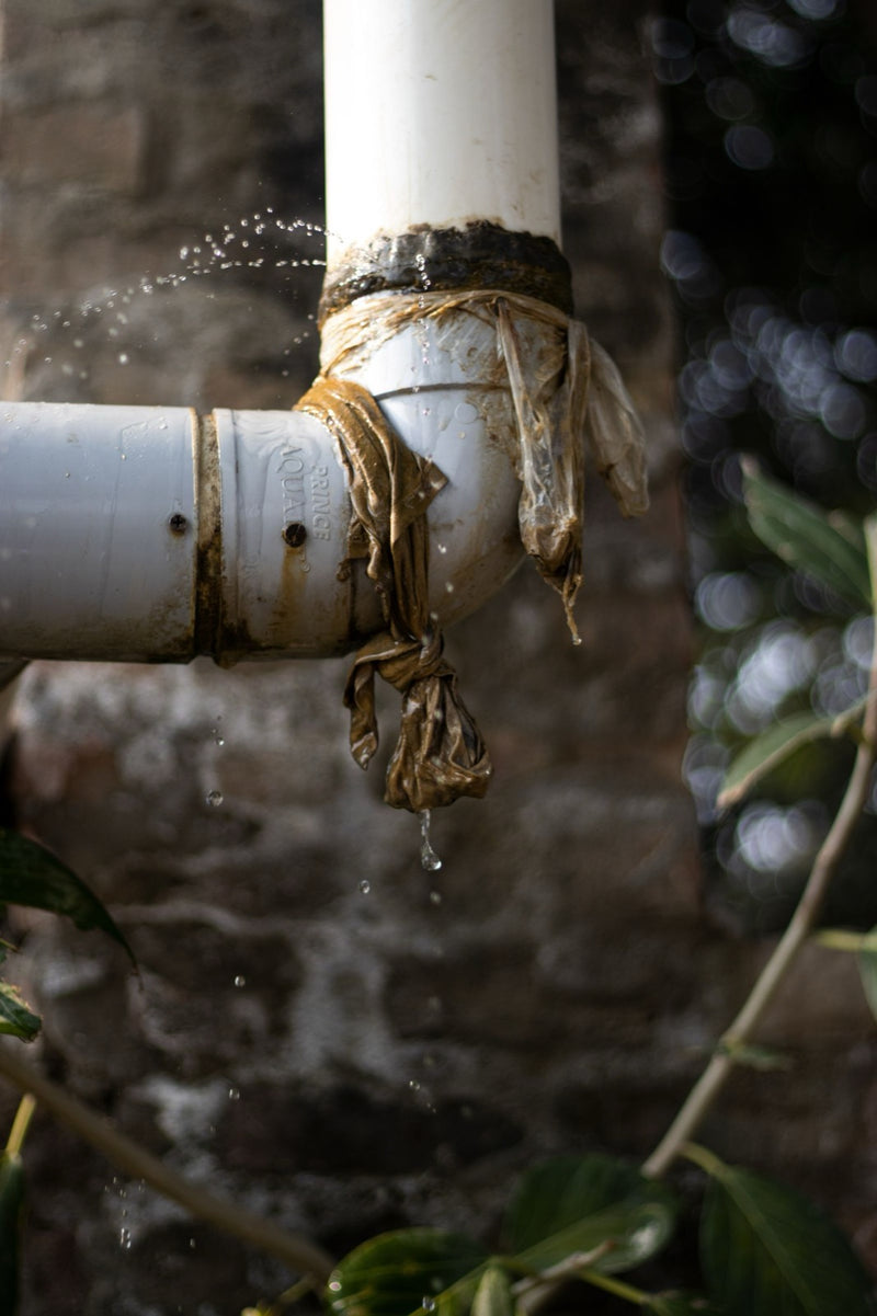 White pipe elbow wrapped in plastic with water spraying and dripping