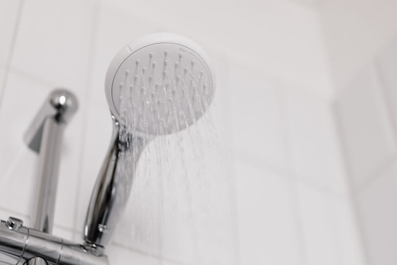 Handheld shower head spraying water in a white tiled shower