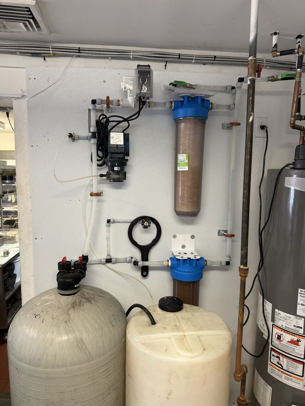 Water softener with sediment and carbon filters on a basement wall, installed by Tucker's Plumbing